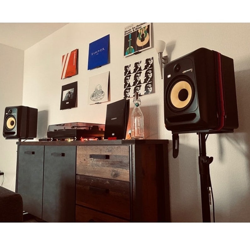 A display made up of six vinyl records on display shelves sits on a wall above a credenza, upon which sits a record player. It's flanked by a pair of speakers