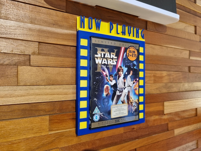 May include: A blue and yellow framed movie display with the words "NOW PLAYING" at the top. The display features a Star Wars movie case. The case has a blue background with images of characters and the title "Star Wars: A New Hope".