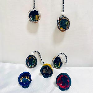 May include: A selection of handmade miniature art pieces. Several are suspended by black and white twine. The pieces include walnut shell pendants with miniature scenes, and small, decorative, eye-shaped and geode-like sculptures.