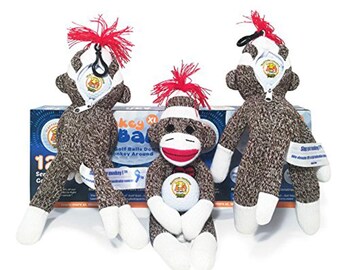 May include: Three sock monkey golf ball holders. The monkeys are wearing white bandages and have red hair. One monkey is holding a white golf ball. The monkeys are sitting in front of a box that says "Monkey Balls Golf Balls Done Monkey Around".
