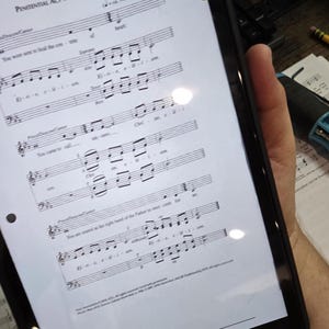 May include: A black tablet displaying sheet music with the title "Penitential Act with Invocations." The tablet is held by a person. The sheet music has musical notes and text.