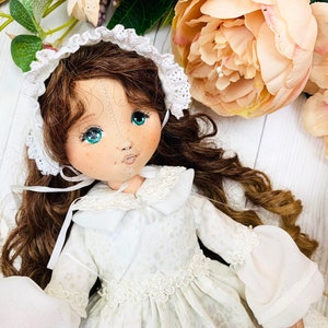 May include: A handmade doll with brown hair, wearing a white dress with lace trim and a white lace bonnet. The doll has blue eyes and a painted face.