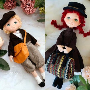 May include: Two handmade cloth dolls. One doll is dressed in a brown jacket, pants, and an orange satchel. The other doll wears a brown dress and holds a colorful patterned bag. Both dolls have hats and painted faces.