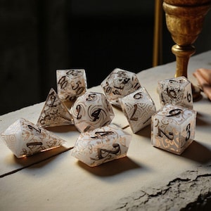 Könnte beinhalten: Eine Sammlung klarer Würfel mit goldfarbenen Akzenten und Zahlen. Die Würfel sind auf einer hellen Oberfläche angeordnet, mit einem dunklen Hintergrund. Die Würfel haben verschiedene Formen, darunter Pyramiden, Würfel und andere polyedrische Formen.