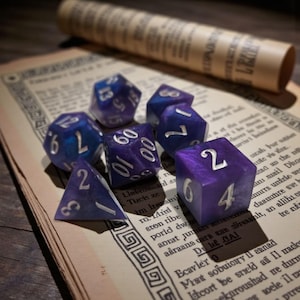 May include: A collection of polyhedral dice in shades of purple and blue with silver numbering, resting on a vintage book page. A rolled-up scroll is in the background. The dice are for tabletop games.
