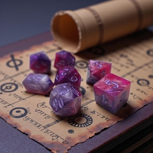 May include: A collection of purple and pink marbled dice with white numbering, scattered on a vintage-style map. A rolled-up parchment tube rests in the background, suggesting a tabletop game theme.