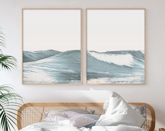 May include: Two framed prints of ocean waves in shades of blue and white hang above a bed with white bedding. The bed has a natural wood headboard and a woven bench at the foot. A potted palm and other decor complete the room.