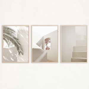 May include: A set of three framed prints featuring a white building with a window, a palm tree, and a set of stairs. The prints are in a minimalist style with a white background and a light beige frame.