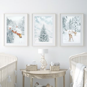 May include: Three framed wall art prints featuring winter scenes: a red train traveling through a snowy forest, a single snow-covered pine tree, and a group of reindeer in a winter landscape. The prints are displayed above a wooden console table.