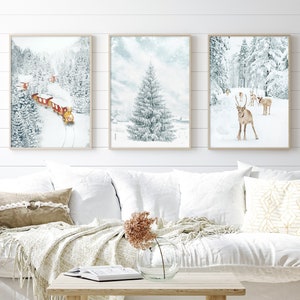 May include: Three framed wall art prints featuring winter scenes. The left print shows a red train in a snowy forest. The center print depicts a snow-covered pine tree. The right print displays a group of reindeer standing in a snowy landscape.