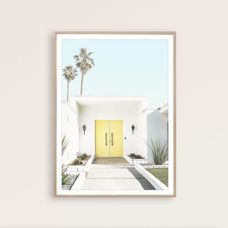 May include: A white mid-century modern house with a bright yellow double door entrance. Palm trees are visible in the background.