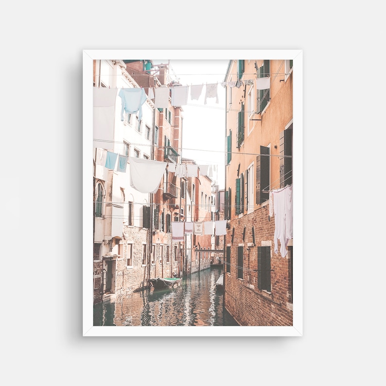 May include: A narrow canal in Venice, Italy, with buildings on either side. White laundry is hanging on lines strung across the canal. A small boat is docked in the water.