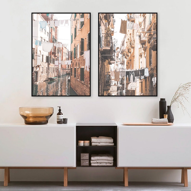 May include: Two framed photographs of narrow streets in Venice, Italy. The photos are in a warm, sepia tone and show buildings with laundry hanging from lines strung across the streets.
