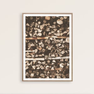 May include: A framed print featuring a close-up view of a neatly stacked pile of firewood. The wood pieces are various shapes and sizes, with a mix of light and dark brown tones. The frame is a light brown color.