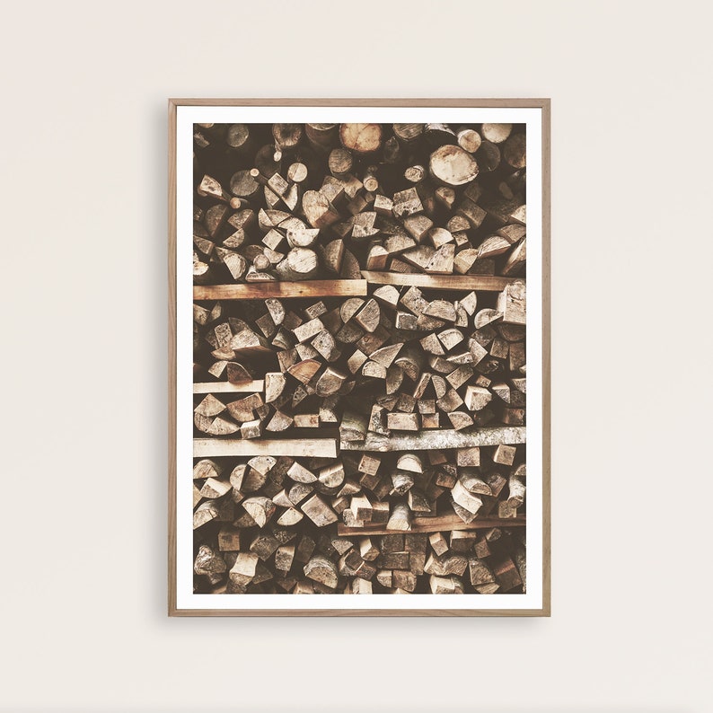 May include: A framed print featuring a close-up view of a neatly stacked pile of firewood. The wood pieces are various shapes and sizes, with a mix of light and dark brown tones. The frame is a light brown color.