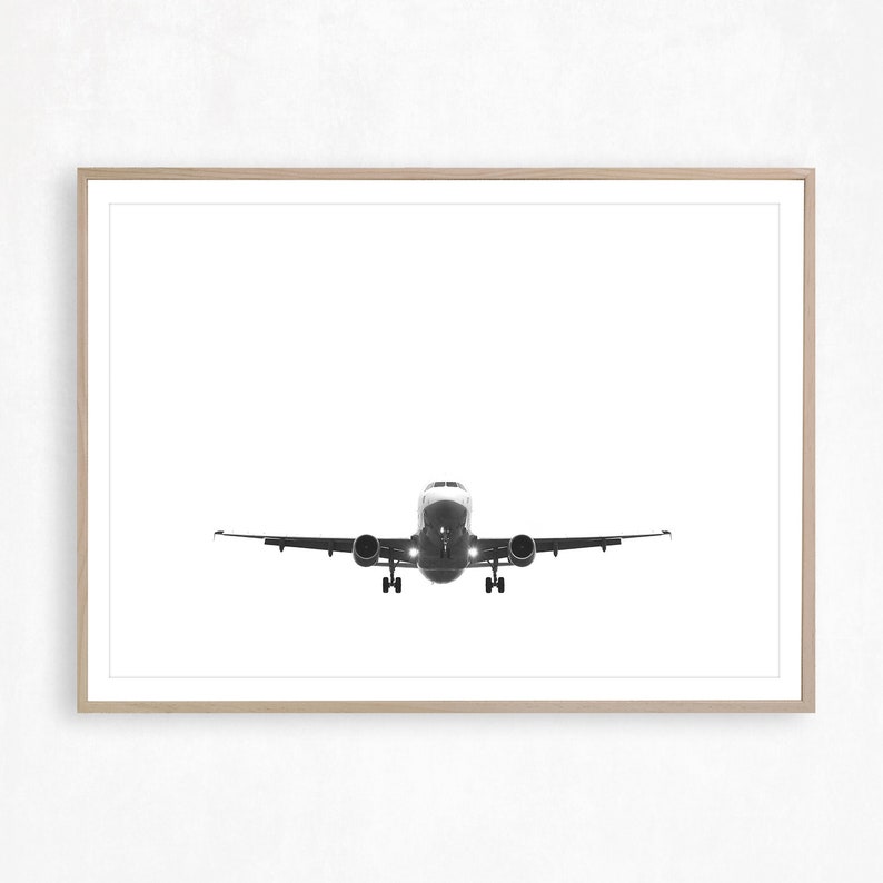 May include: A monochrome photograph of an aeroplane in flight, centrally positioned. The plane is viewed head-on, with its wings spread. The image is framed in a light-coloured wooden frame, set against a white background.