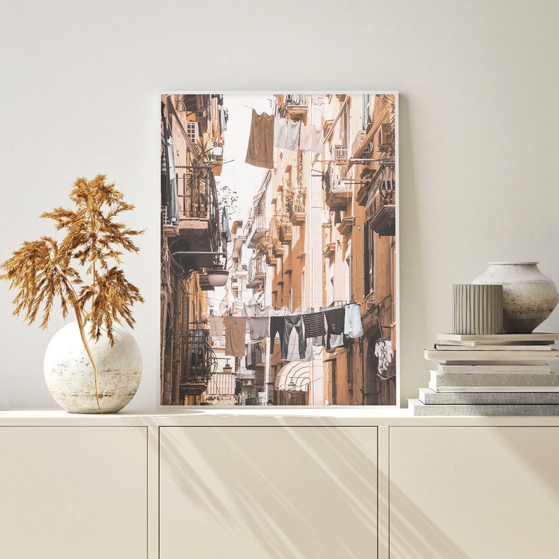 May include: A photograph of a narrow street in a city with buildings on both sides. The buildings are painted in shades of beige and brown. Laundry is hanging on lines strung across the street.