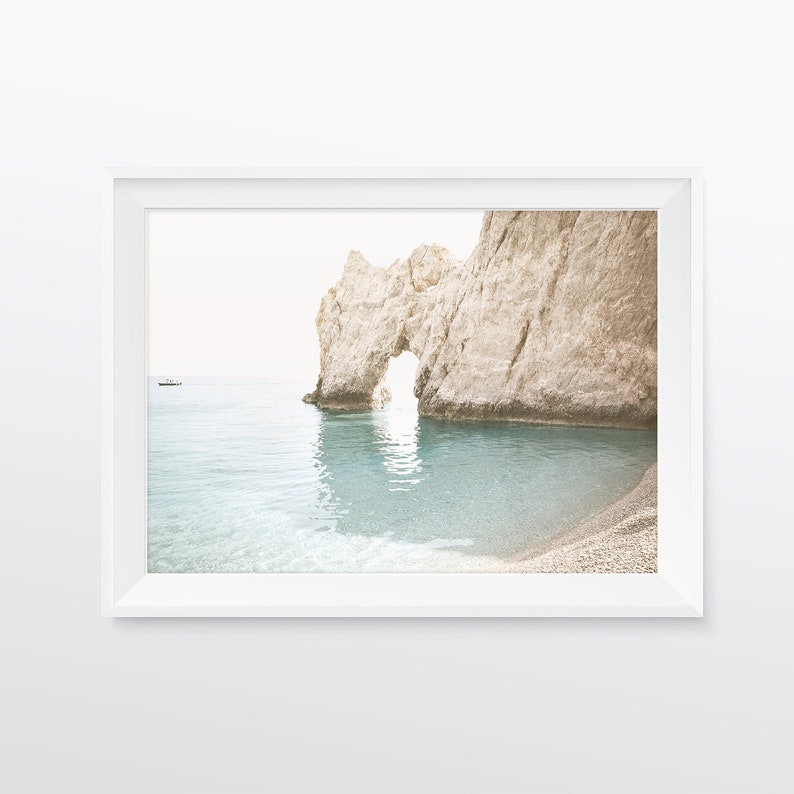 Puede incluir: Una formaci&oacute;n rocosa blanca con un arco natural crea un marco para una vista de un oc&eacute;ano azul turquesa y una playa de arena.