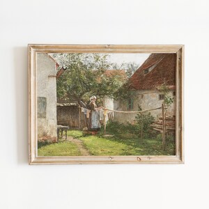 May include: A framed oil painting depicting a woman hanging laundry on a clothesline in a rural setting. The woman is wearing a white apron and a blue dress. The scene is set in a backyard with a whitewashed building and a green tree in the background.