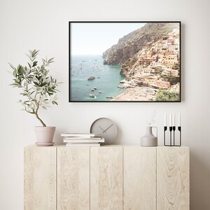 May include: A framed photograph of a coastal town with colorful buildings built into a cliffside. The town is situated on a bay with a clear blue sea and many boats. The photo has a vintage, faded look.