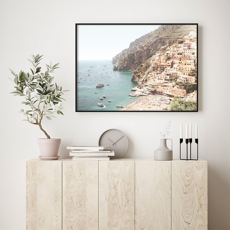 May include: A framed photograph of a coastal town with colorful buildings built into a cliffside. The town is situated on a bay with a clear blue sea and many boats. The photo has a vintage, faded look.