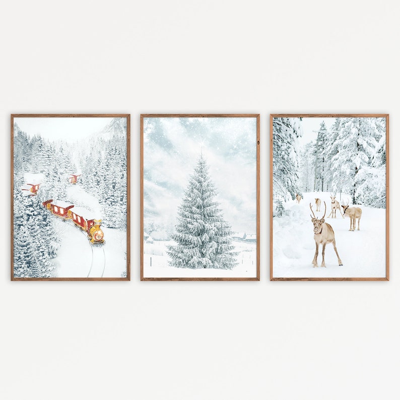 May include: A set of three framed wall art prints featuring winter scenes. The first shows a red train in a snowy forest, the second a snow-covered pine tree, and the third a group of reindeer standing in a white, frost-covered landscape.