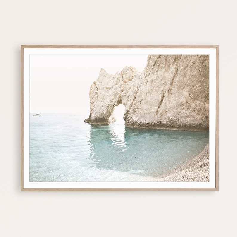 Puede incluir: Una fotograf&iacute;a enmarcada de un arco rocoso sobre un oc&eacute;ano turquesa. El arco est&aacute; hecho de roca de color claro y el agua est&aacute; tranquila y clara. El cielo es de un blanco suave.