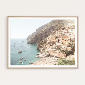 May include: A colorful cityscape built into a cliffside overlooking a turquoise ocean with boats and a sandy beach. The buildings are a mix of yellow, orange, and red, and the sky is a light blue.