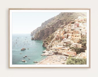 May include: A colorful cityscape built into a cliffside overlooking a turquoise ocean with boats and a sandy beach. The buildings are a mix of yellow, orange, and red, and the sky is a light blue.