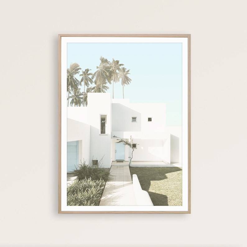 May include: A white modern house with a blue door and palm trees in the background. The house has a walkway leading to the front door.