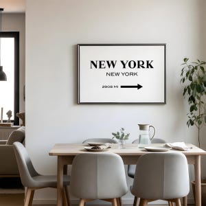 May include: A rectangular wall art print in a thin black frame featuring the text NEW YORK, NEW YORK and 2908 MI with a black arrow pointing to the right. The print has a white background with bold black lettering in a clean, sans-serif font.