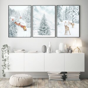 May include: A set of three framed wall art prints featuring winter scenes. The left print shows a red train in a snowy forest, the center print depicts a large pine tree in a snowy landscape, and the right print displays reindeer in the snow.