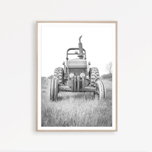 May include: A black and white photograph of a vintage tractor in a field. The tractor is facing the camera and has a large exhaust pipe.