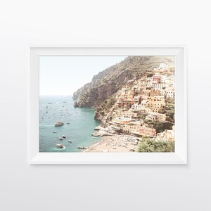 May include: A panoramic view of a colorful town built on a steep cliffside overlooking a turquoise ocean. The town is filled with white buildings with red tile roofs, and there are many boats in the water.