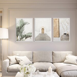 May include: Three framed prints with minimalist designs. The left print features a green palm tree, the center print shows a white archway with a golden door and steps, and the right print has a brown vase with a dried branch.