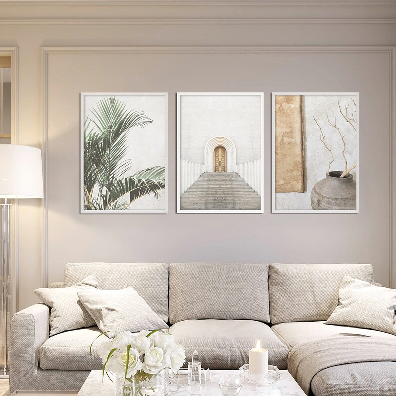 May include: Three framed prints with minimalist designs. The left print features a green palm tree, the center print shows a white archway with a golden door and steps, and the right print has a brown vase with a dried branch.