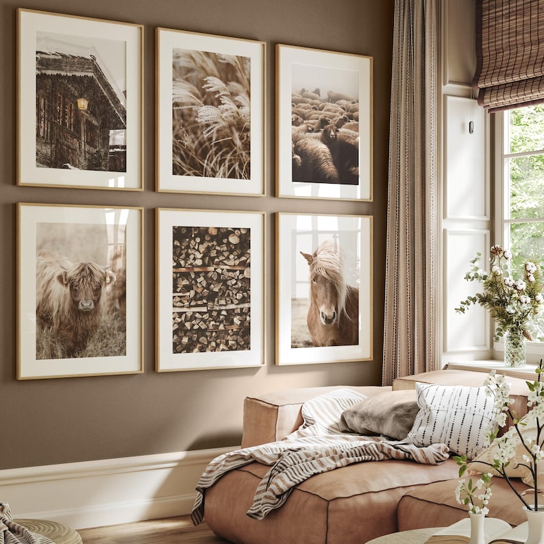 May include: Six framed art prints with gold frames. The prints feature a snowy cabin, tall grass, a flock of sheep, a Highland cow, stacked firewood, and a horse. The art has a neutral color palette.