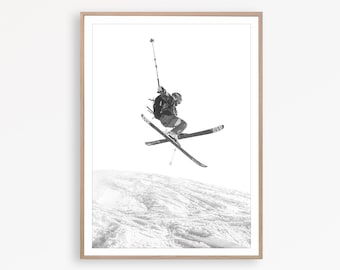 May include: A black and white photograph of a skier in mid-air, performing a trick on skis. The skier is wearing a helmet and a backpack. The skier is against a white background with a snowy mountain in the distance.