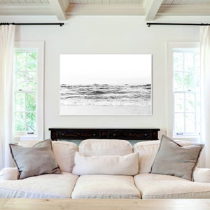 May include: A large rectangular wall art print featuring a black and white photograph of ocean waves crashing onto a sandy beach. The horizon line is clear, and the image displays high contrast between the dark water and the bright white sky.