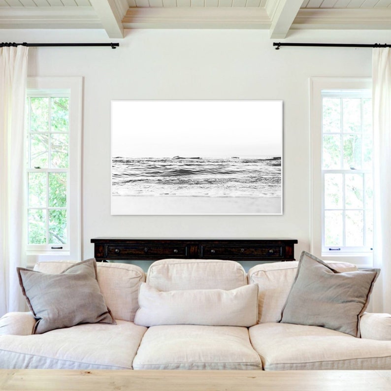 May include: A large rectangular wall art print featuring a black and white photograph of ocean waves crashing onto a sandy beach. The horizon line is clear, and the image displays high contrast between the dark water and the bright white sky.
