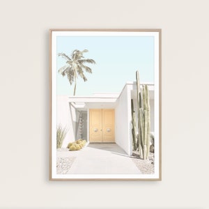 May include: A white modern house with a yellow double door entrance. The house is surrounded by a small garden with palm trees and cacti.