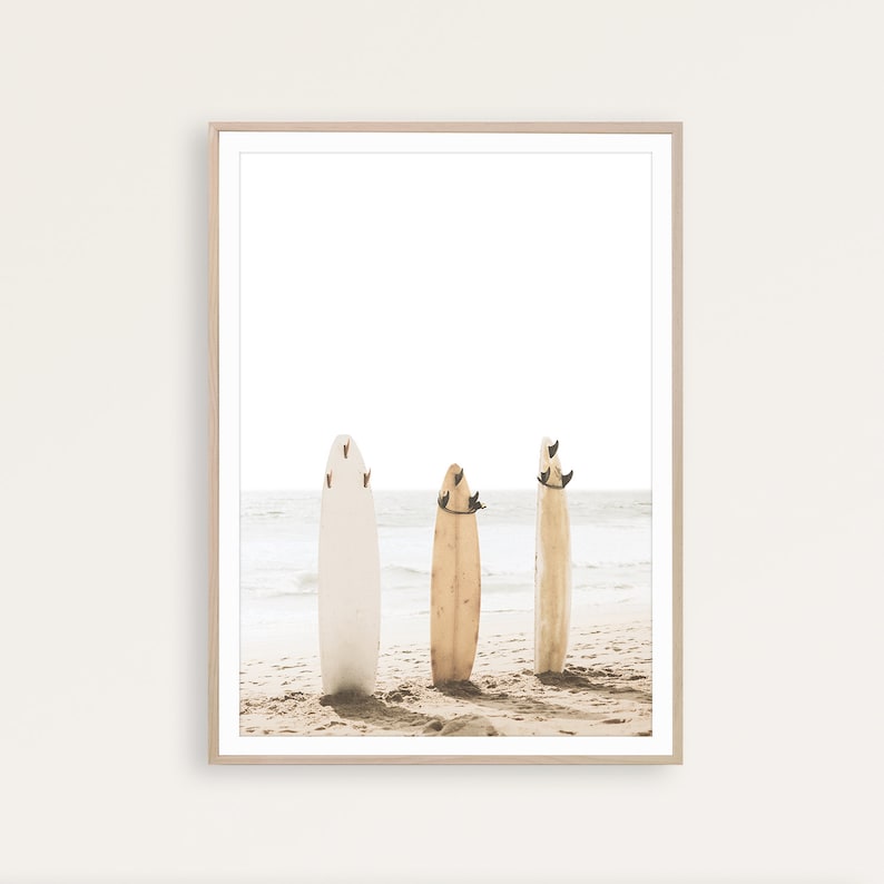 Puede incluir: Tres tablas de surf est&aacute;n de pie en una playa de arena. Las tablas de surf son de diferentes colores, una blanca, otra marr&oacute;n y otra beige. Las tablas de surf est&aacute;n todas apoyadas la una en la otra, y la playa est&aacute; vac&iacute;a.
