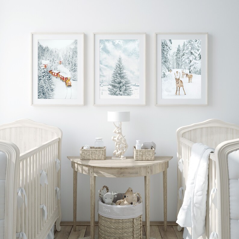May include: Three framed wall art prints featuring winter scenes: a red train traveling through a snowy forest, a single snow-covered pine tree, and a group of reindeer in a winter landscape. The prints are displayed above a wooden console table.