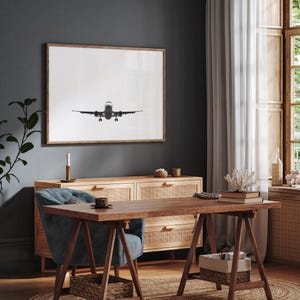 May include: A monochrome framed print of an aircraft in mid-flight, displayed above a wooden sideboard. The room includes a desk, chair, and a window with natural light, contributing to a contemporary interior design.