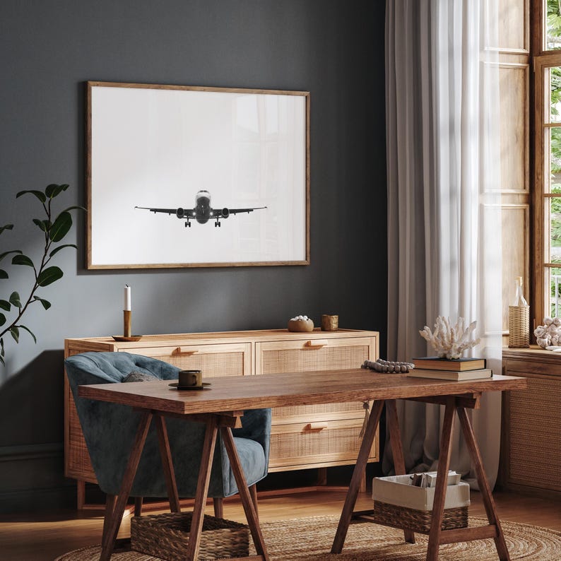 May include: A monochrome framed print of an aircraft in mid-flight, displayed above a wooden sideboard. The room includes a desk, chair, and a window with natural light, contributing to a contemporary interior design.