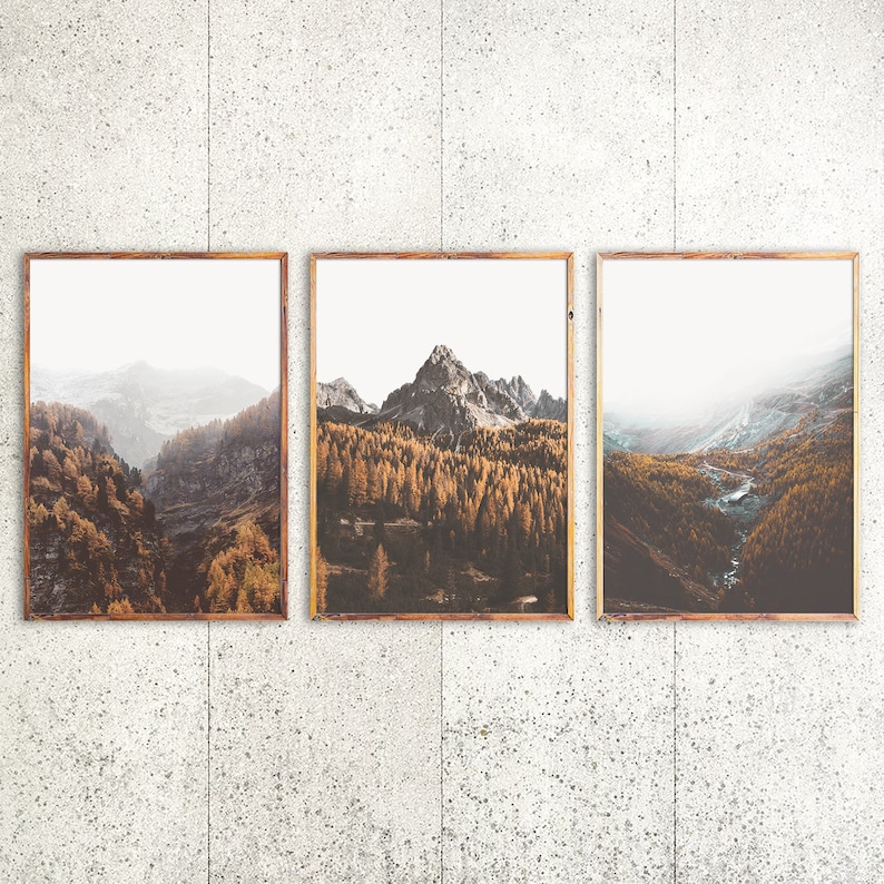 May include: A set of three rectangular wall art prints in thin wooden frames, each displaying a landscape photograph of a mountain range covered in golden autumn trees, rocky peaks, and misty valleys under a bright, overcast sky.