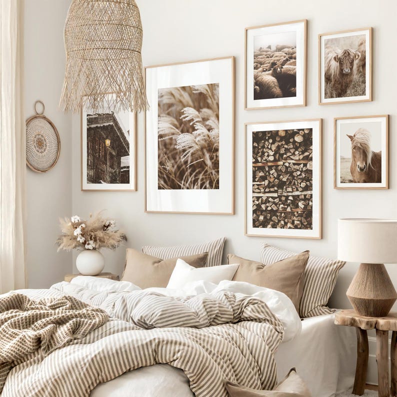 May include: A bedroom with a neutral color palette, featuring framed art prints of nature scenes. The prints include images of tall grass, a cabin, sheep, a horse, and stacked firewood. The bed is made with striped bedding and decorative pillows.