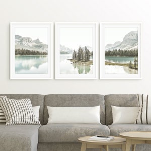 May include: Three framed landscape photographs of a lake with mountains in the background. The lake is a light blue color and the mountains are a light gray color. The photos are all in white frames.