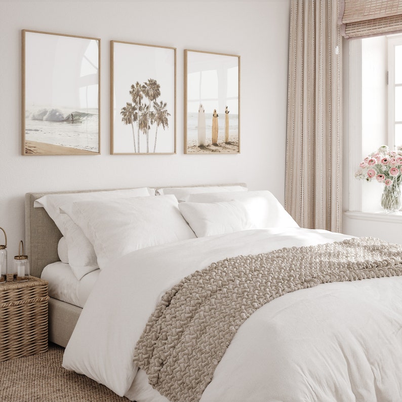 Puede incluir: Una cama blanca con una manta de punto beige y almohadas blancas. Tres impresiones enmarcadas de escenas de playa cuelgan en la pared detr&aacute;s de la cama.