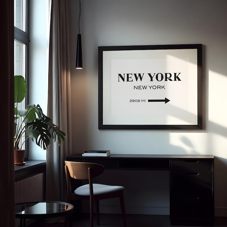 May include: A framed wall art print featuring the text NEW YORK in large bold letters, followed by NEW YORK in smaller text, and 2908 MI with a right-pointing arrow. The print is displayed in a black frame against a light-colored wall.
